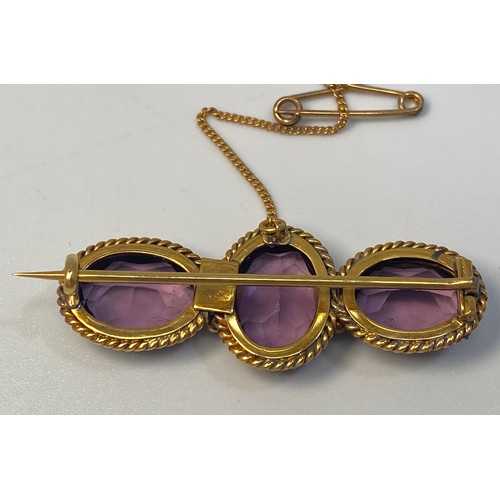 218 - A yellow metal (tests as 14 or 15ct) brooch set with three oval faceted amethyst coloured stones in ... 