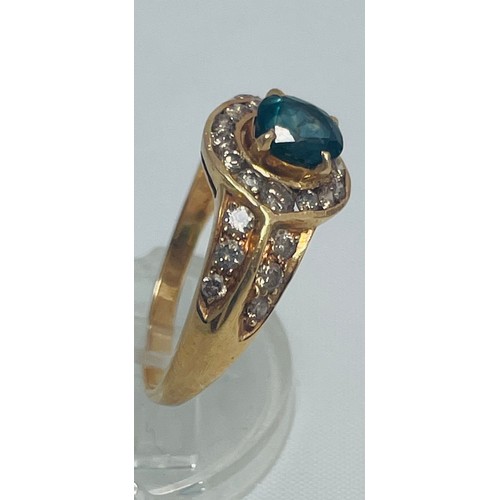 194 - An 18ct yellow gold dress ring, set with an oval blue faceted stone to the centre with 14 x small di... 