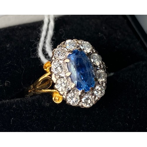 273 - An 18ct gold ring, centrally claw set with an oval faceted sapphire coloured stone, surrounded by te... 