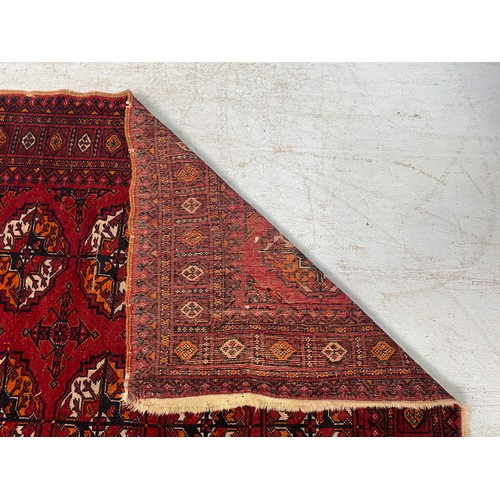 616 - A Caucasian hand-knotted woollen carpet, the central claret field with rows of guls, and a continuou... 