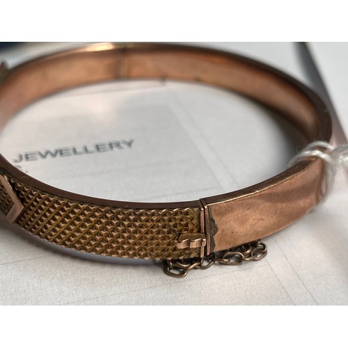 318 - A 9ct gold bangle, designed as a buckle to the top, with safety chain, weighs 10.9 grams.

The top o... 