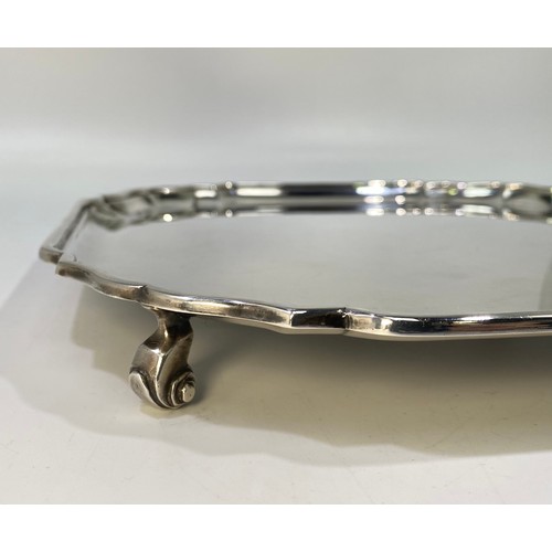 162 - A ERII silver salver of square form with serpentine canted corners, pie-crust rim raised on four scr... 