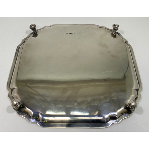 162 - A ERII silver salver of square form with serpentine canted corners, pie-crust rim raised on four scr... 