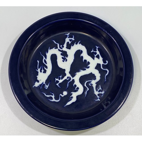 101 - A Chinese porcelain 'scarificial blue' dragon dish, with white reserved dragon to richly applied dee... 