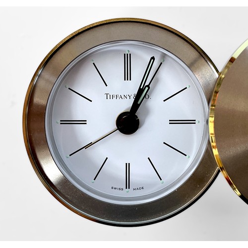 106 - A Tiffany & Co white metal travel alarm clock with yellow metal trim, swivel cover reveals white ena... 