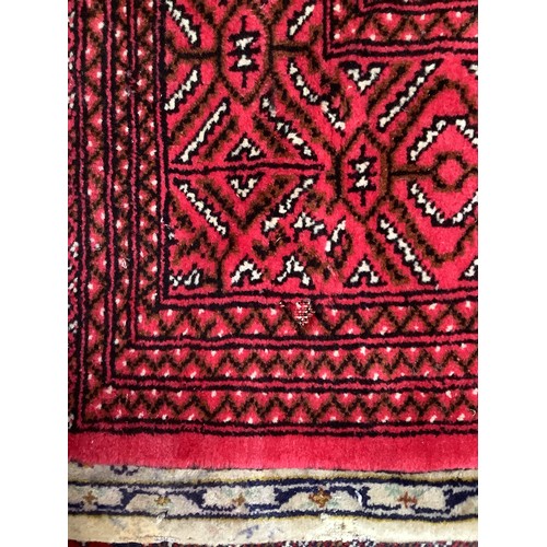 408 - A hand-knottd woollen Bokhara carpet, typically worked with a field of stylised guls to a red ground... 