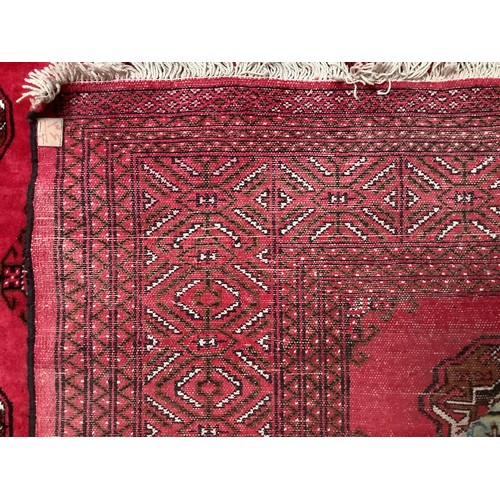 408 - A hand-knottd woollen Bokhara carpet, typically worked with a field of stylised guls to a red ground... 