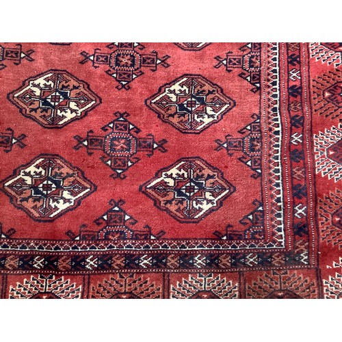 409 - A hand-knotted wool Bokhara carpet, typically worked with stylised guls to a red ground within a bor... 