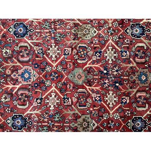 413 - A hand-knotted wool garden carpet, with with a field of stylised flowers to deep red ground, within ... 