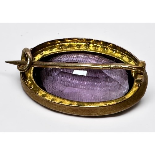 122 - A 9ct gold brooch, centrally set with a large faceted amethyst coloured stone, surrounded by seed pe... 