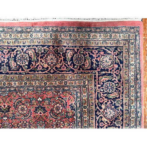 406 - A large rouge ground hand-knotted Persian carpet, worked with a dense field of stylised polychrome f... 