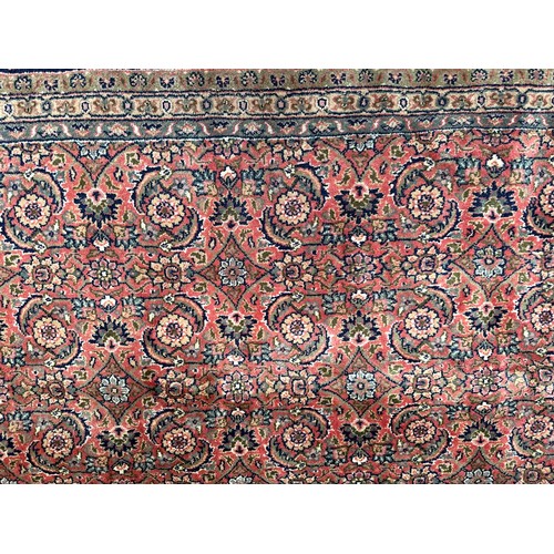 406 - A large rouge ground hand-knotted Persian carpet, worked with a dense field of stylised polychrome f... 