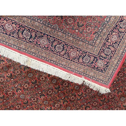 406 - A large rouge ground hand-knotted Persian carpet, worked with a dense field of stylised polychrome f... 