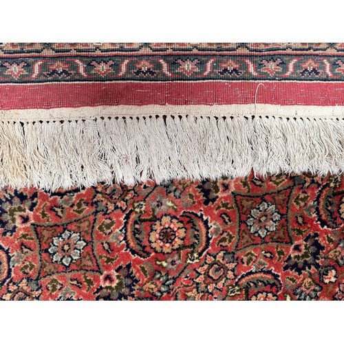 406 - A large rouge ground hand-knotted Persian carpet, worked with a dense field of stylised polychrome f... 