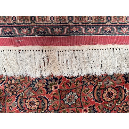 406 - A large rouge ground hand-knotted Persian carpet, worked with a dense field of stylised polychrome f... 