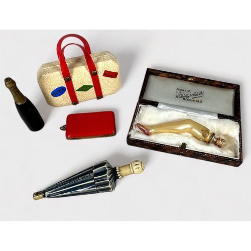 380 - Five Novelty Needle Cases, comprising a suitcase, red purse, champagne bottle, glass leg with gold s... 