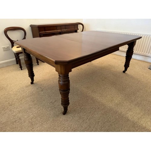 706 - A large Victorian mahogany dining table, two leaves, canted corners, raised on four turned supports ... 