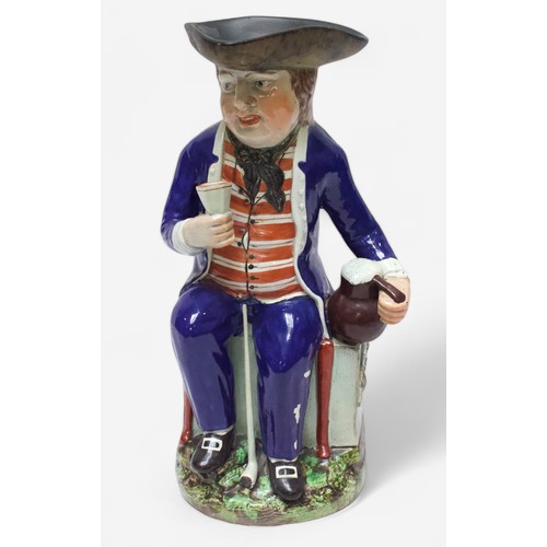 33 - A Prattware ‘Sailor’ toby jug, c1810, with blue frock coat and matching britches, a long tobacco pip... 