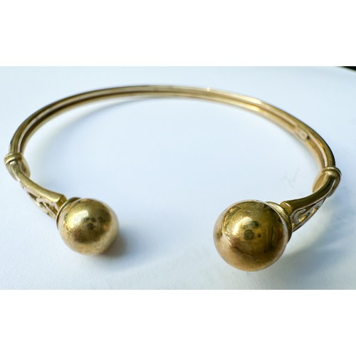 75 - A 9ct yellow gold torque bangle with pierced pattern and gold ball ends, weighs 5.8 grams.