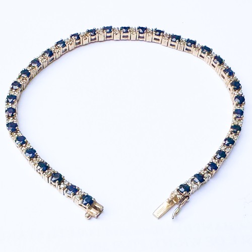 79 - A 9ct yellow gold line bracelet, set with thirty-four round sapphires, with two small round diamonds... 