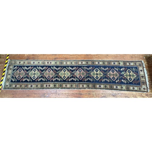 132 - A hand-knotted Caucasian runner worked with eight stylised guls to a blue field within stylised flor... 