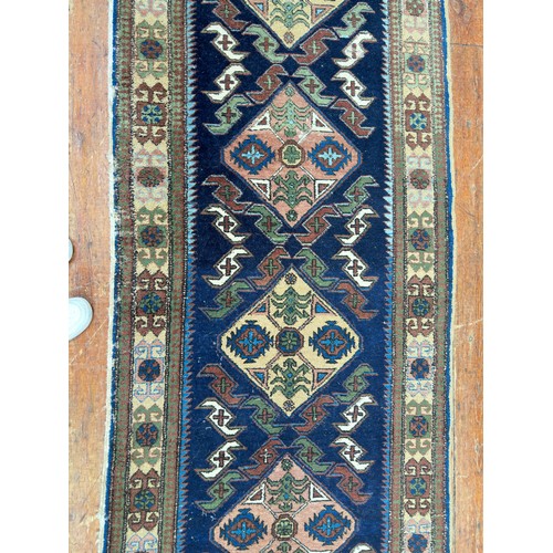 132 - A hand-knotted Caucasian runner worked with eight stylised guls to a blue field within stylised flor... 