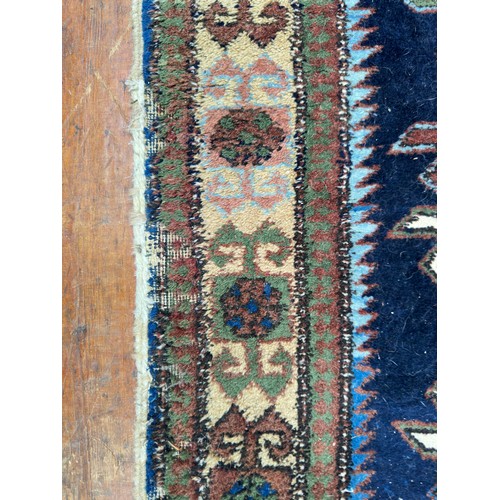 132 - A hand-knotted Caucasian runner worked with eight stylised guls to a blue field within stylised flor... 