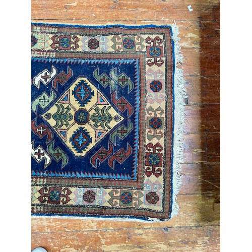 132 - A hand-knotted Caucasian runner worked with eight stylised guls to a blue field within stylised flor... 