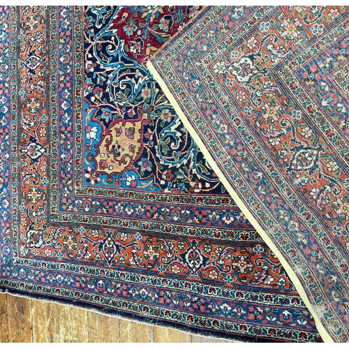 135 - A large Persian hand-knotted medallion carpet worked with deep rouge and reds, stylised floral spand... 