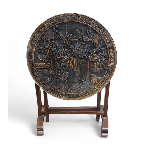 190 - A Chinese hardwood gate-leg tilt-top occasional table, the top ornately carved with figures in a lan... 