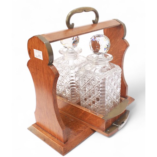 243 - An early 20th Century oak and brass two-bottle tantalus, with swivel mechanism, housing two hobnail ... 