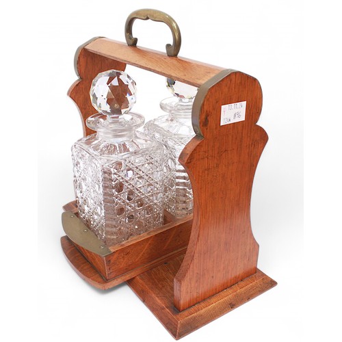 243 - An early 20th Century oak and brass two-bottle tantalus, with swivel mechanism, housing two hobnail ... 