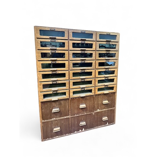 643 - An oak and oak veneered haberdashery cabinet, of three banks of drawers with glazed fronts and hand-... 