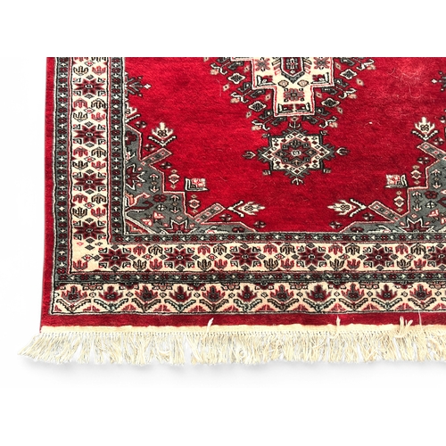 488 - A hand-knotted woollen rug, worked with a stylised central medallion to a bright red ground, within ... 