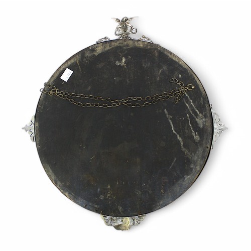 496 - A Victorian silvered brass circular mirror, bevelled glass, the frame surmounted with applied putti ... 