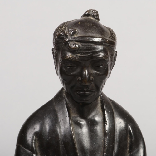 184 - A Japanese Meiji period bronze statue raised on a wooden plinth. Formed as a man holding a pipe and ... 