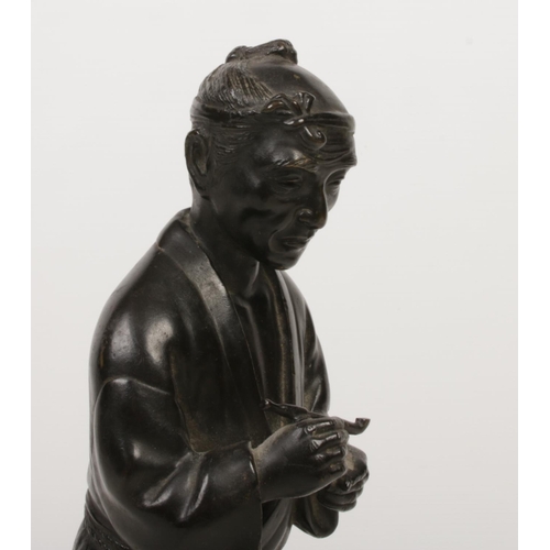 184 - A Japanese Meiji period bronze statue raised on a wooden plinth. Formed as a man holding a pipe and ... 