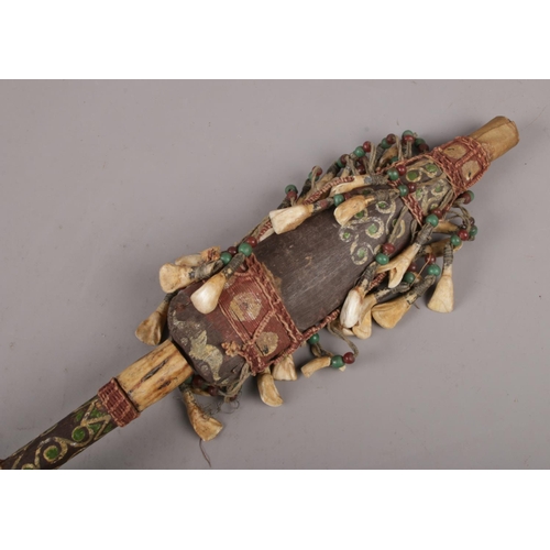 147 - An African tribal witch doctor stick, with animal tooth and pigment decoration. (Length 94cm).