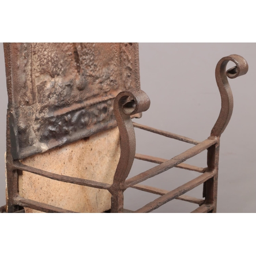 80 - An 18th century wrought iron fire grate. The arch top back decorated in relief with a figure and rai... 