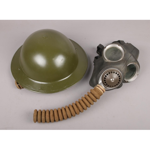 A military Brodie type helmet along with a WWII gas mask stamped