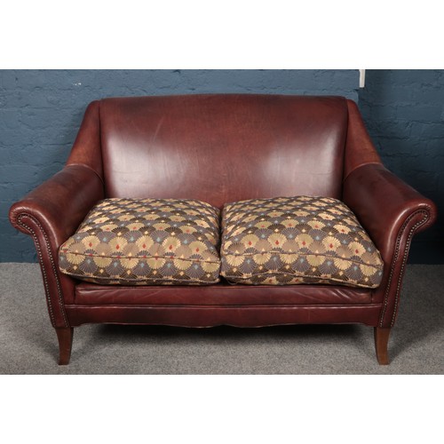 438 - A brown leather two seater sofa, with Liberty style cushions.