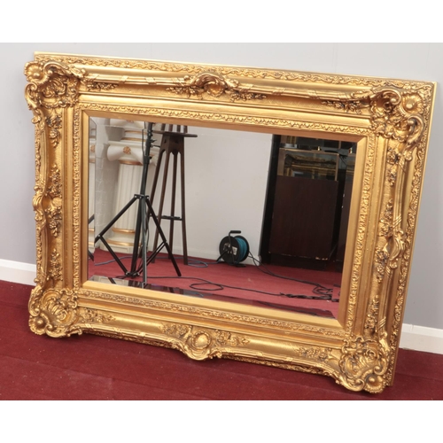 377 - A large ornate gilt framed bevel edge wall mirror. (101cm x 130cm)