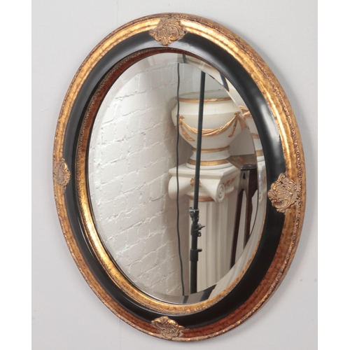 381 - An oval gilt and black framed bevel edge wall mirror. (66cm x 52cm)