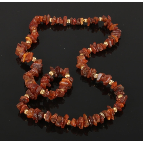 597 - A prehistoric raw cognac amber bead and yellow metal necklace 74cm long.