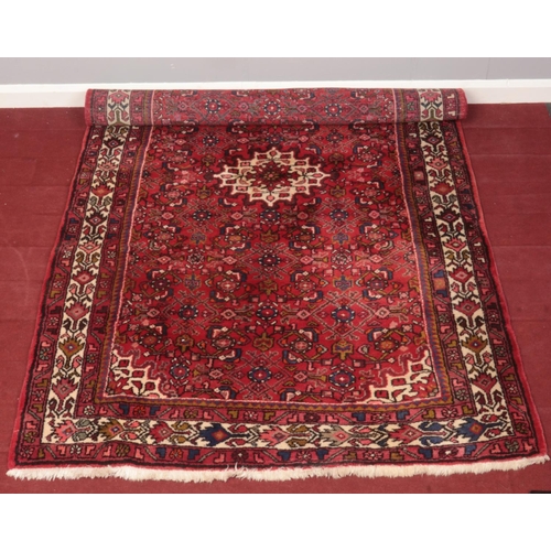 373 - A red ground wool rug with central medallion design. (216cm x 134cm)