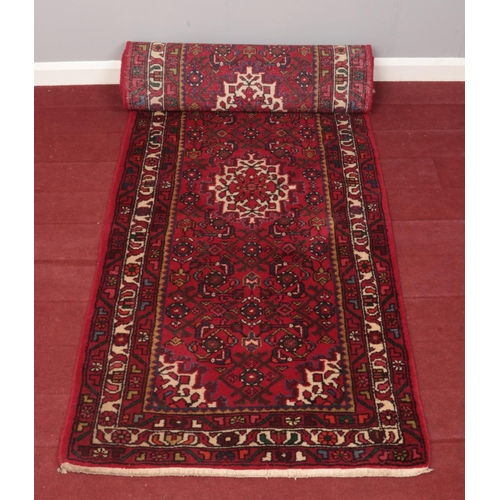 375 - A red ground wool runner with medallion motifs. (338cm x 83cm)