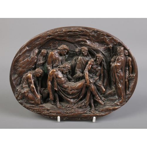 316 - An oval cast metal plaque depicting Jesus descending from the cross. Signed Justin. H:15cm W:20cm.