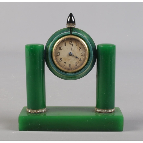 131 - An Art Deco travelling clock in case. Possibly green bakelite housing a gilt metal timepiece.