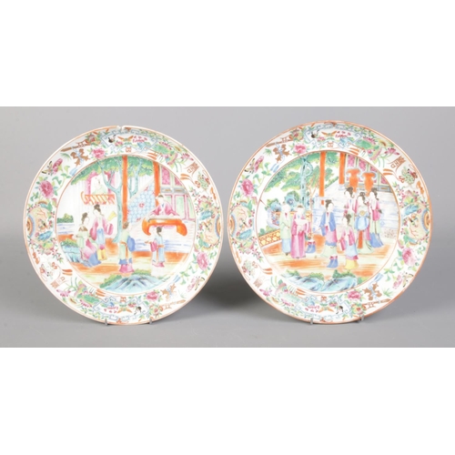 96 - A pair of Cantonese famille rose plates, both decorated with figures on a terrace. 25cm diameter.