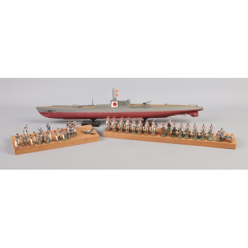 100 - A collection of hand painted war figures, mounted on board together with a model Japanese submarine.